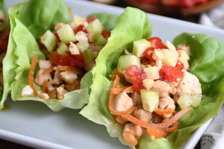 Top down view of lettuce leaves full of a chicken vegetable mixture on a white plate.