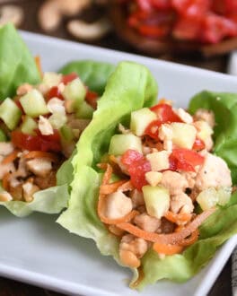 Top down view of lettuce leaves full of a chicken vegetable mixture on a white plate.