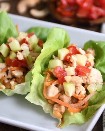 Top down view of lettuce leaves full of a chicken vegetable mixture on a white plate.