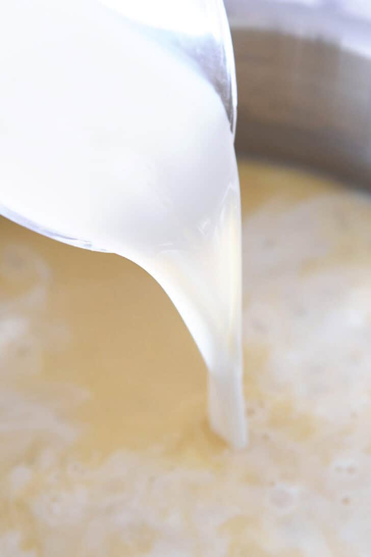 Milk being poured into a pot of white sauce.