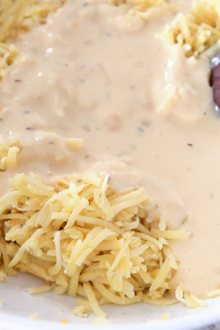 Top down view of shredded cheese and white sauce being mixed together in a white dish.