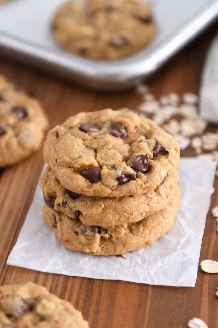 Three brown butter pumpkin oatmeal chocolate chip cookies stacked on square of parchment paper.