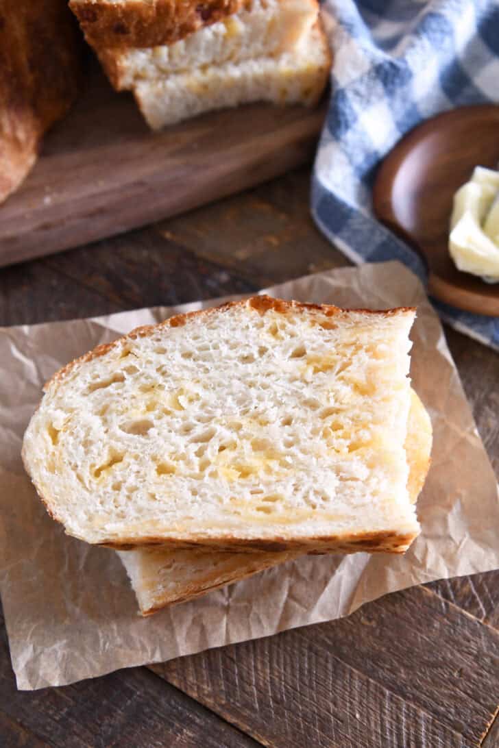 Top down view of half slice of cheesy peasant bread on brown parchment paper.