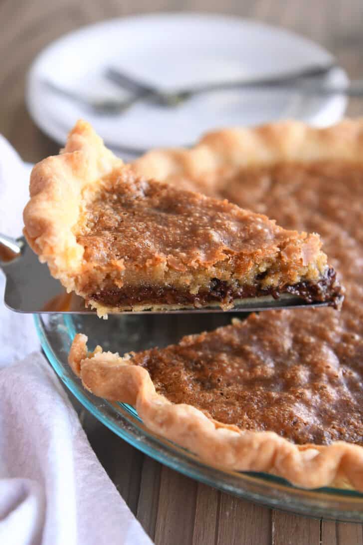 A metal spatula taking out a slice of chocolate chip cookie pie from the rest of the pie.