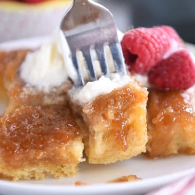 A fork taking a bite out of a caramelized french toast bake on a white plate.