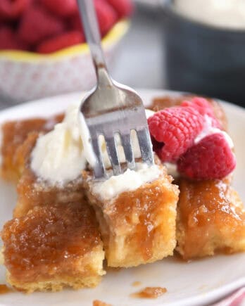 A fork taking a bite out of a caramelized french toast bake on a white plate.