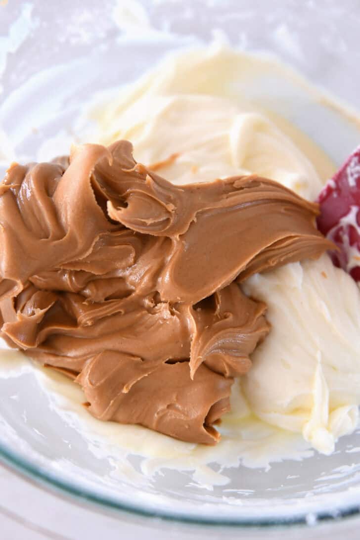 Top down view of a glass bowl with peanut butter and a creamy white mixture.
