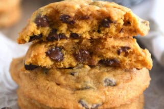 Pumpkin chocolate chip cookies stacked on top of each other with the top cookie split in half.