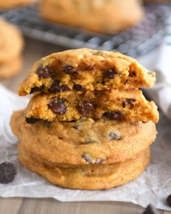 Pumpkin chocolate chip cookies stacked on top of each other with the top cookie split in half.