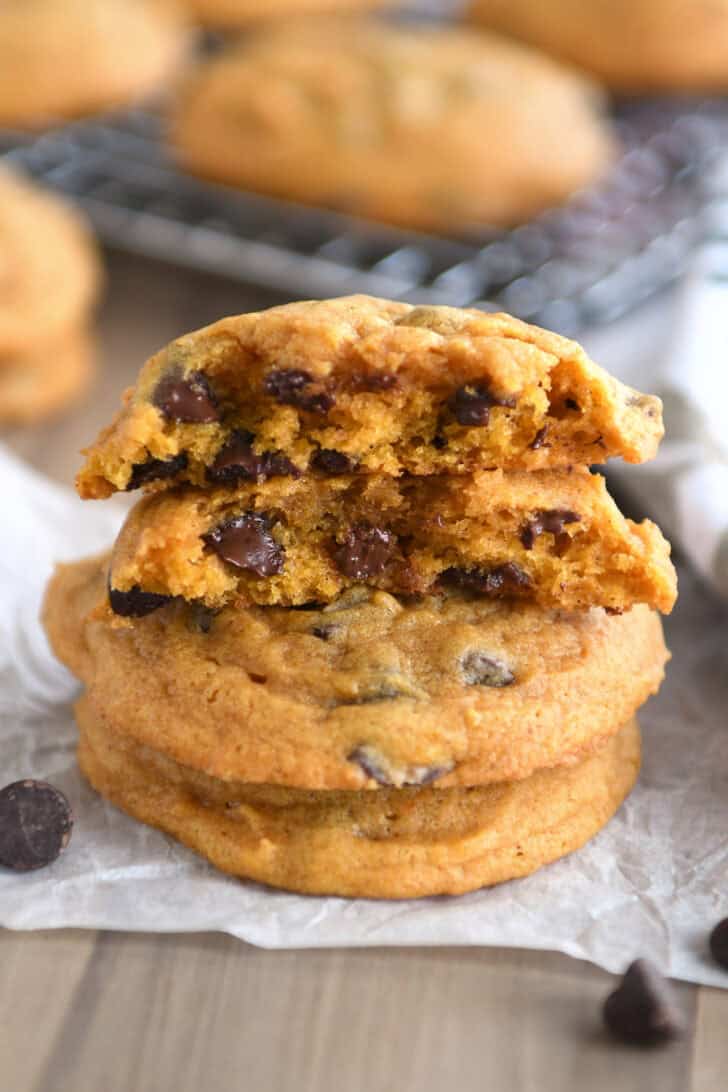 Pumpkin chocolate chip cookies stacked on top of each other with the top cookie split in half.