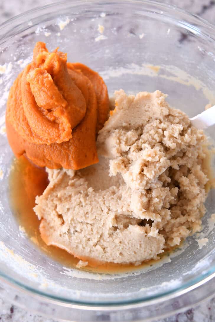Top down view of a glass bowl filled with brown sugar and butter that has been mixed together and a large dollop of pureed pumpkin.