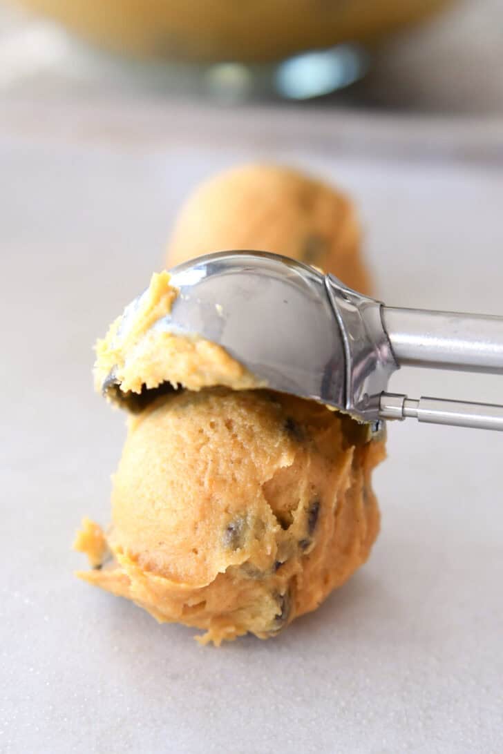 A cookie scoop dropping a ball of pumpkin chocolate chip cookie dough onto a piece of parchment.