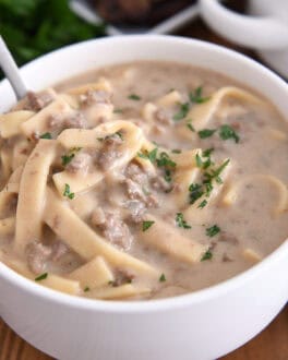 Spoon in bowl with beef stroganoff soup topped with fresh parsley.