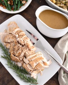 White platter with cooked turkey, rosemary, gravy boat, stuffing and green beans.