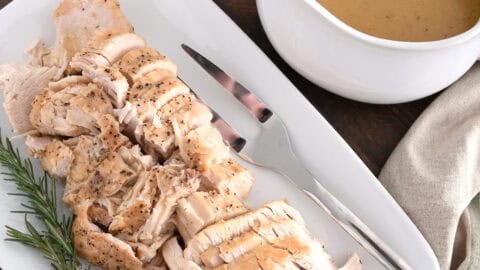 White platter with cooked turkey, rosemary, gravy boat, stuffing and green beans.