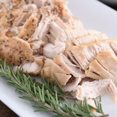 Cooked turkey on white platter with rosemary.