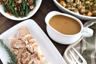 Top down view of platters of turkey, rosemary, gravy, stuffing, green beans and mashed potatoes.