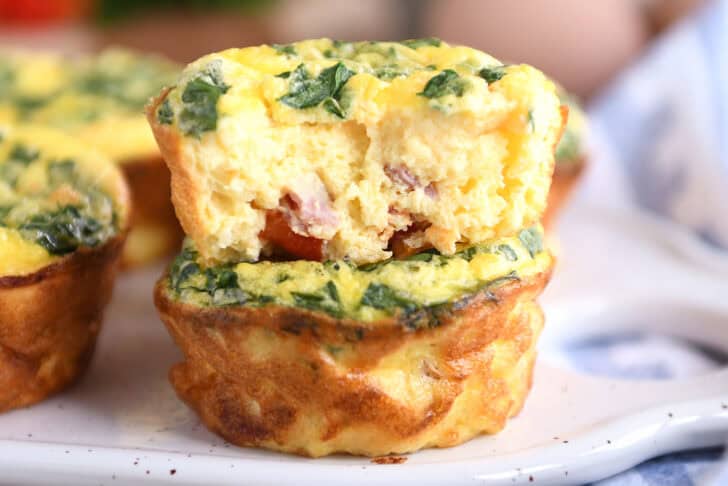 Two cooked egg and veggie muffins cups stacked on top of each other with a bite taken out of the top egg muffin.