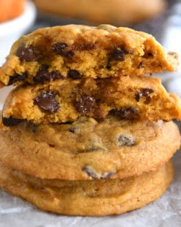 Pumpkin chocolate chip cookies stacked on top of each other with the top cookie split in half.