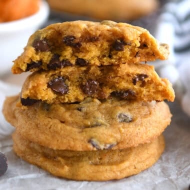 Pumpkin chocolate chip cookies stacked on top of each other with the top cookie split in half.