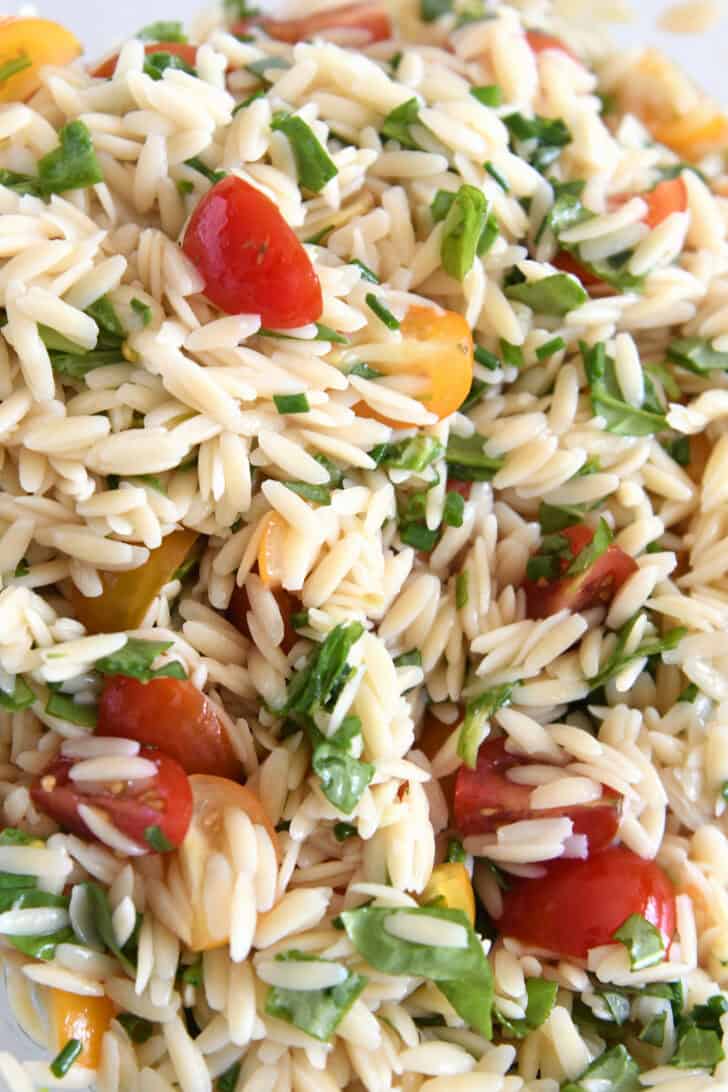 Top down view of a cooked orzo salad with halved cherry tomatoes and chopped basil.
