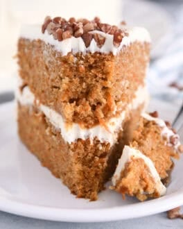 Place a slice of carrot layer cake on a white plate with a bite on a fork.