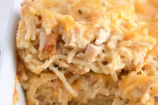 Spatula holding square of cheesy chicken spaghetti in white pan with the rest of the casserole.