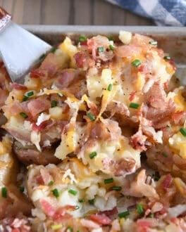 Square spatula scooping portion of cheesy smashed potatoes off of half sheet pan.