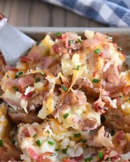 Spatula scooping cheesy mashed potatoes from half sheet pan.