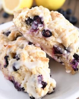 Two baked and glazed lemon blueberry scones on white plate.