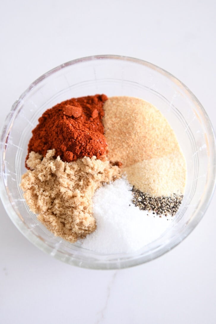Smoked paprika, garlic powder, onion powder, brown sugar, salt and pepper in a glass bowl.