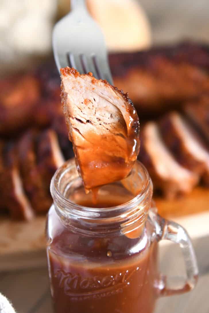 Cooked pork tenderloin with fork spread in barbecue sauce.