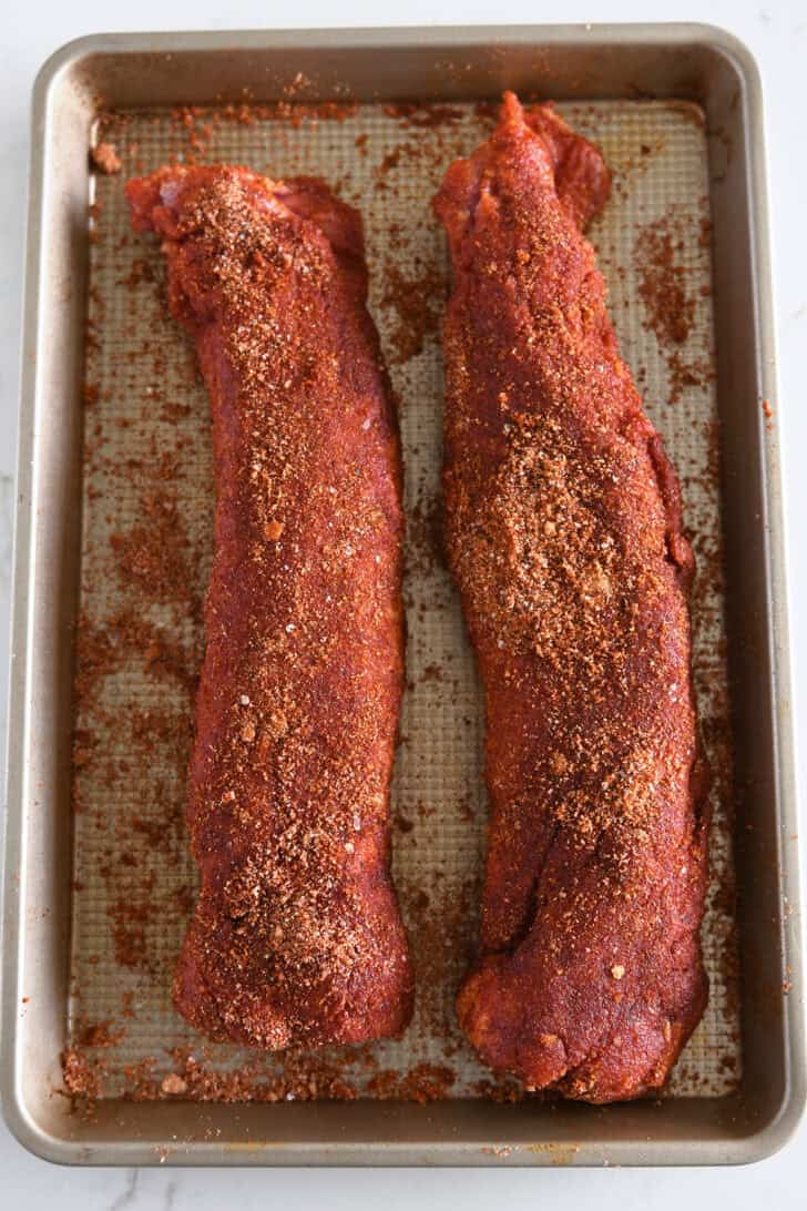 Top-down view of two spice shell pork tenderloin on golden baking tray.