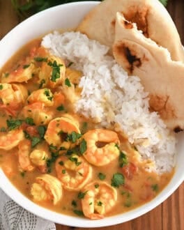 Top down view of a white bowl with flatbread, white rice, and shrimp in a curry sauce.