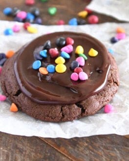 One chocolate cookie spread with chocolate ganache and sprinkled with rainbow chips on white parchment paper.