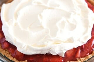 A strawberry pie with graham cracker crust in glass pie plate with whipped cream on top.
