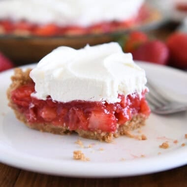 Half eaten slice of strawberry pie with whipped cream on top on white plate.