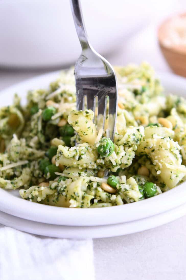 A white plate with pesto pasta salad with peas and shredded parmesan.
