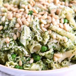 Pesto pasta salad topped with pine nuts in a white bowl.