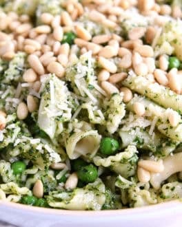 Pesto pasta salad topped with pine nuts in a white bowl.