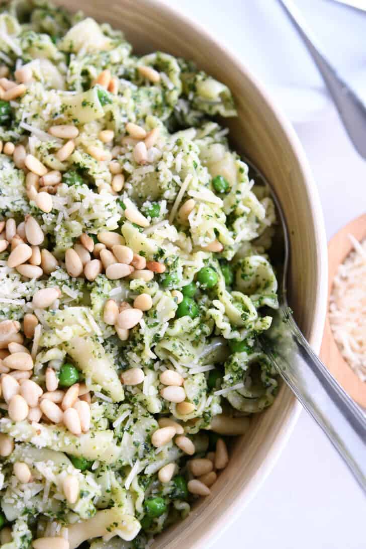 Top down view of a pesto pasta salad topped with pine nuts in a wooden bowl.
