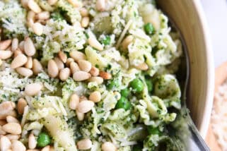Top down view of a pesto pasta salad topped with pine nuts in a wooden bowl.