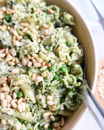 Top down view of a pesto pasta salad topped with pine nuts in a wooden bowl.