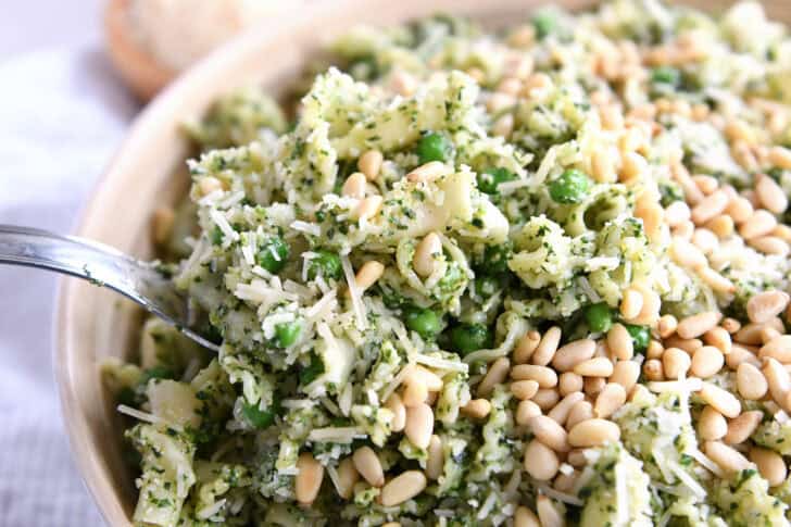 A pesto pasta salad topped with pine nuts and shredded parmesan cheese in a wooden bowl.
