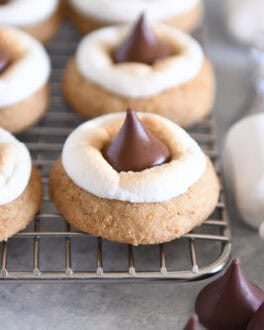 Assembled s'mores blossom cookies with toasted marshmallows and Hershey's Kisses on cooling rack.