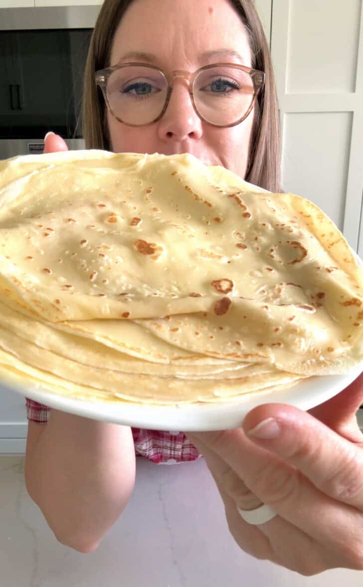Woman holding plate of cooked crepes.