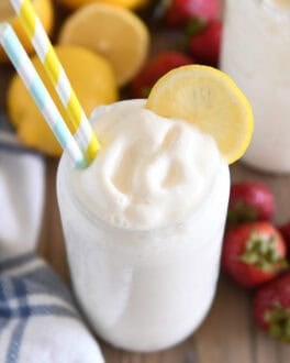 Tall glass filled with frosted lemonade with striped straws and lemon slice for garnish.