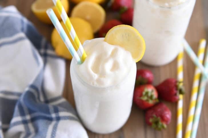 Tall glass filled with frosted lemonade with striped straws and lemon slice for garnish.