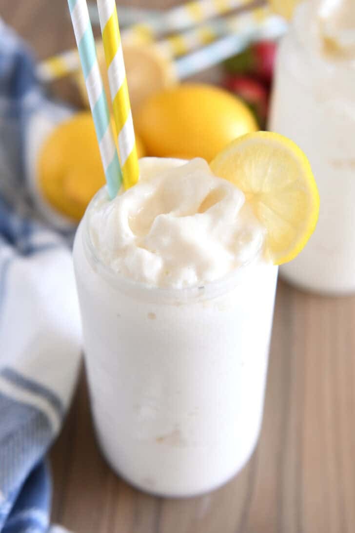 Tall glass filled with frosted lemonade with striped straws and lemon slice for garnish.