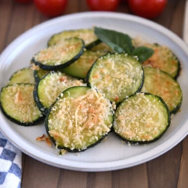 Thinly sliced baked zucchini rounds on plate topped with panko bread crumbs and Parmesan cheese.